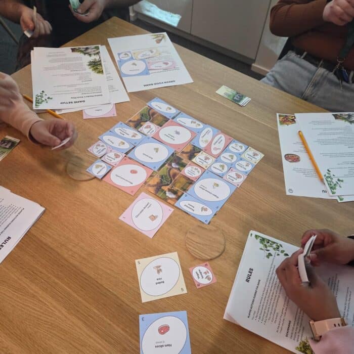 Neljä henkilöä pelaa uutta planetaarista ruokapeliä pöydän äärellä.