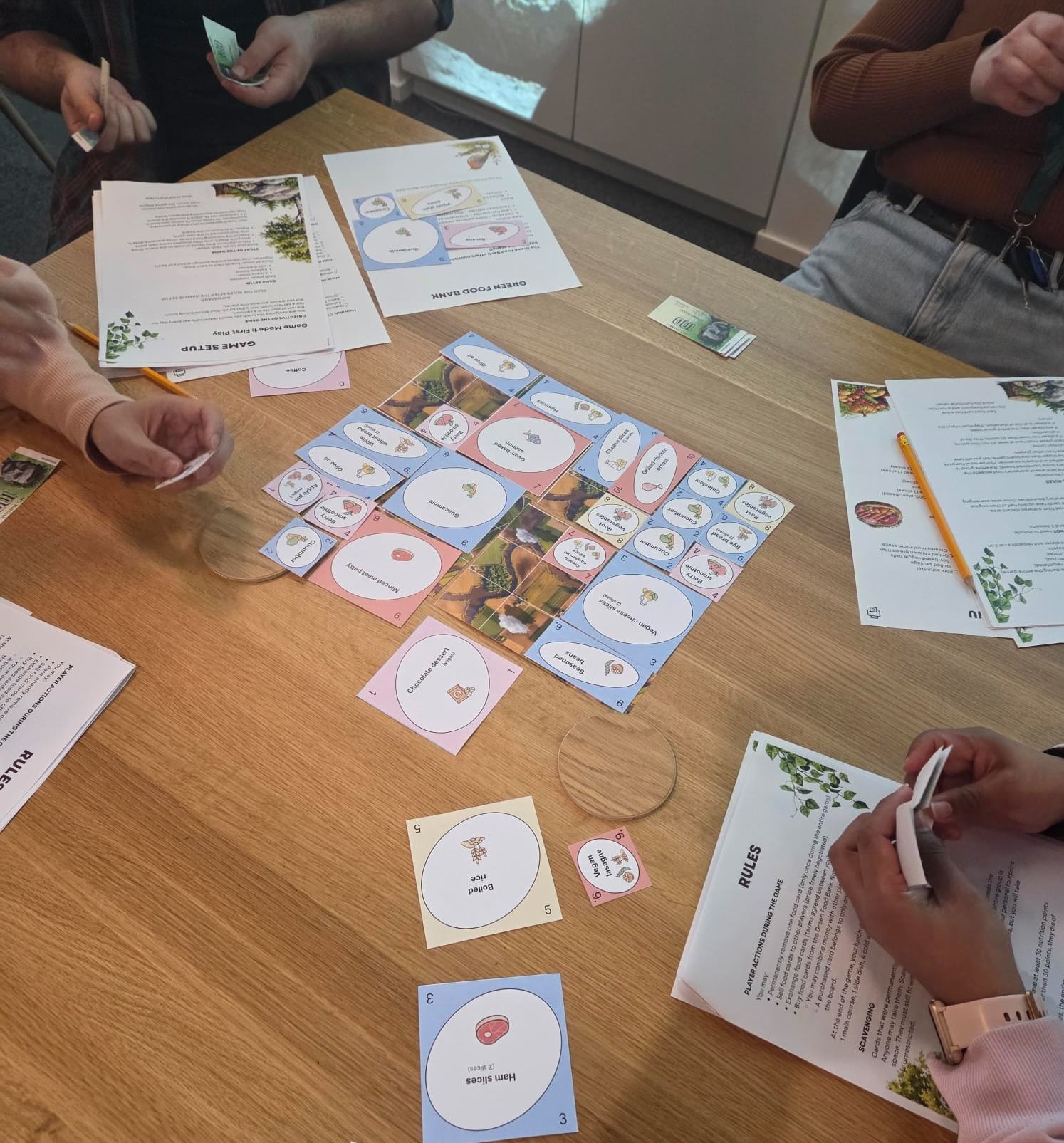 Neljä henkilöä pelaa uutta planetaarista ruokapeliä pöydän äärellä.